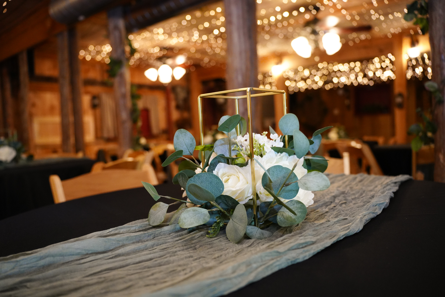 geometric golden reception table centerpiece with white flowers sitting atop a sage green table runner and a black table cloth at Honeysuckle Hills