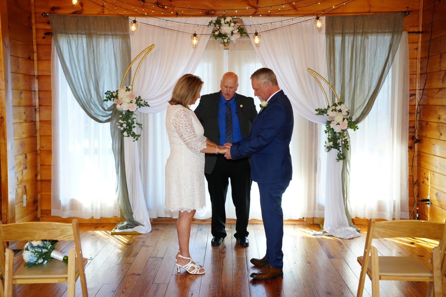 Wedding couple praying during their ceremony in a wedding chapel with white and green swag curtains and string lights