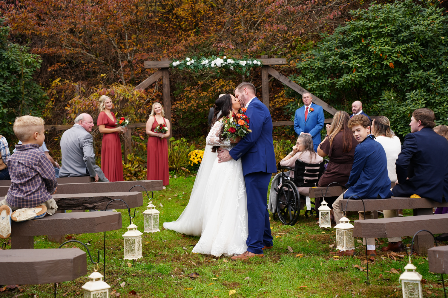 peak fall leaf color surrounding a couple kissing after their forest themed wedding ceremony at a wooden arbor at Honeysuckle Hills